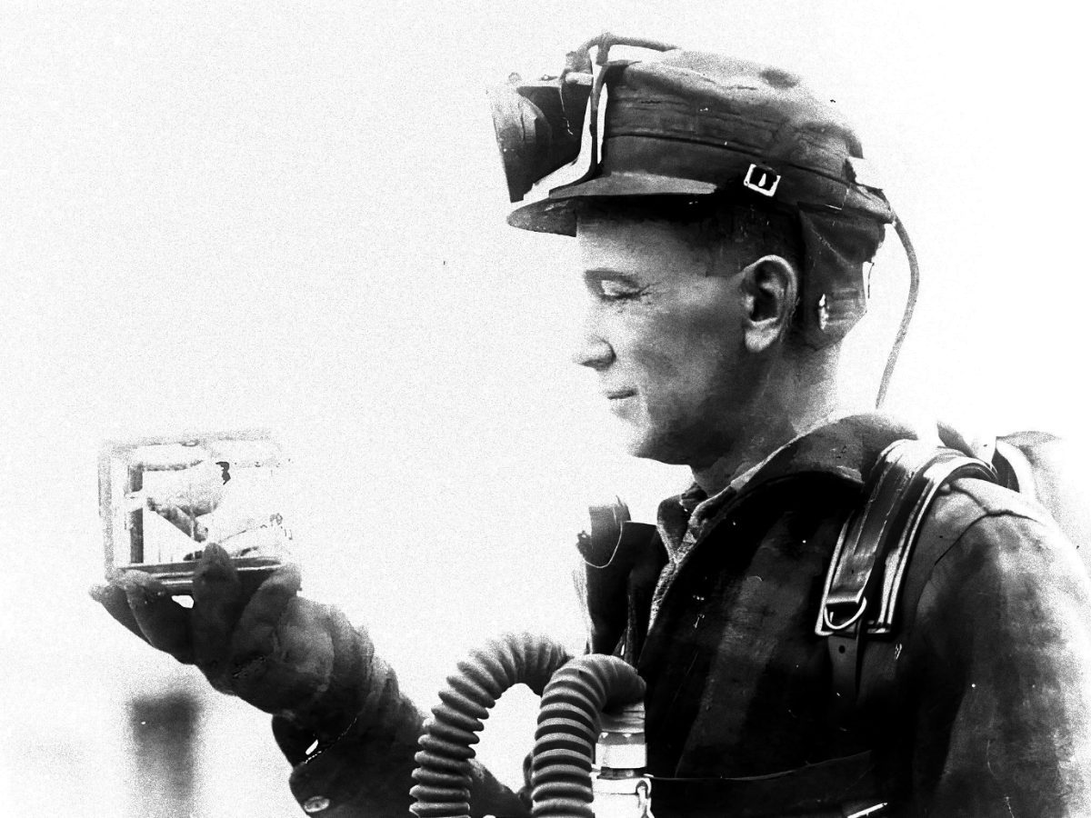 A coal miner holding a canary in a cage